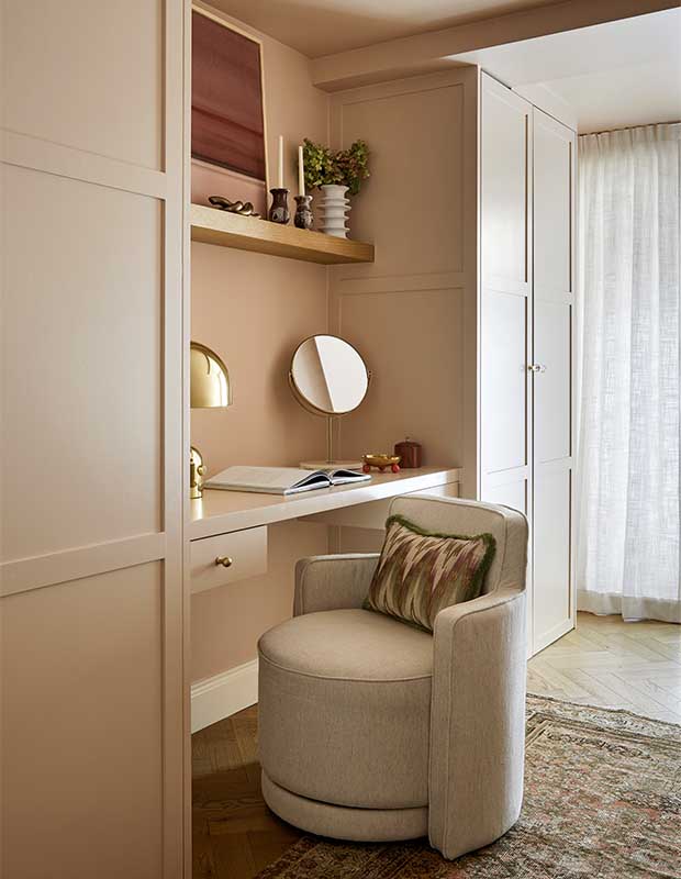 A peach-rose coloured dressing room with shiny gold accents including lamps. A thick round chair sits at the desk, and the linen curtains allow natural light in. notting hill flat